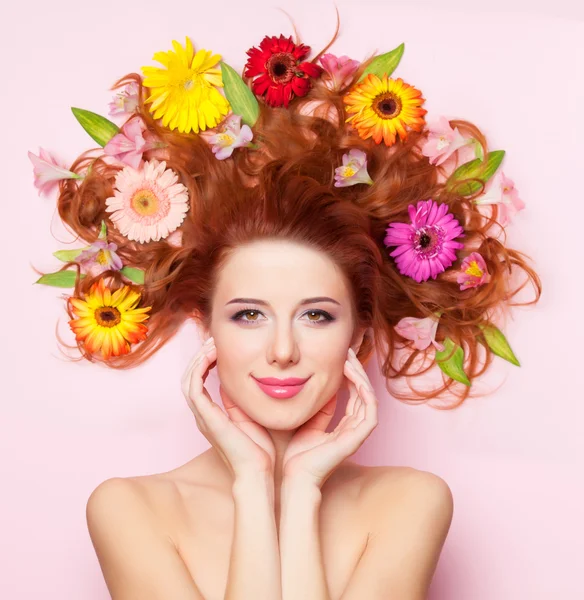Vacker rödhårig flicka med blommor på rosa bakgrund — Stockfoto