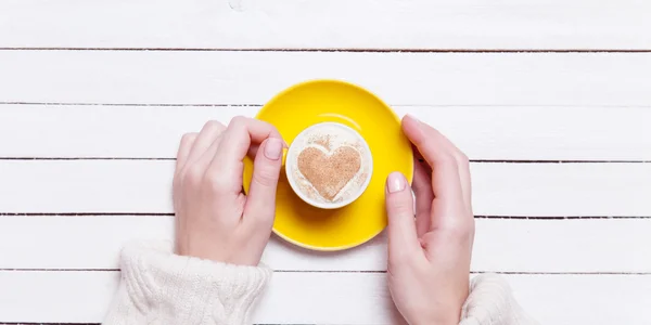 Kvinnliga händer som håller kopp kaffe på träbord. — Stockfoto