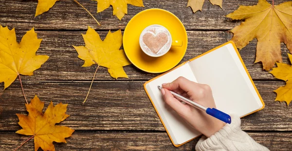 Kvinnlig hand skriva något i anteckningsboken nära kopp kaffe. — Stockfoto