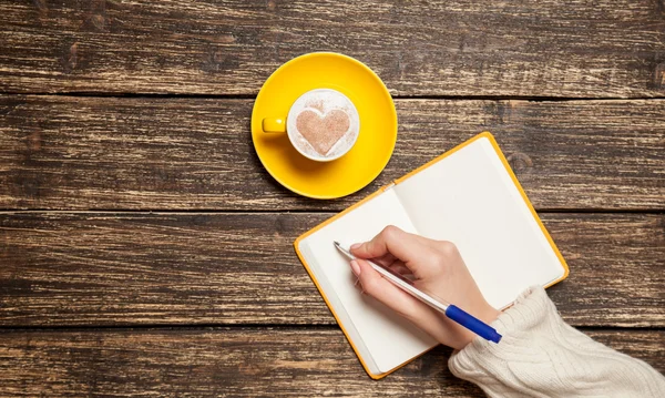 女性的手，写一些东西在附近杯咖啡的笔记本. — 图库照片