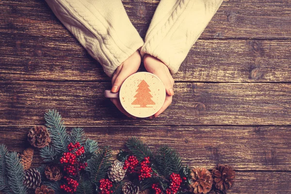 Female holding cup of coffee with cream christmas tree on a tabl — Stock Photo, Image