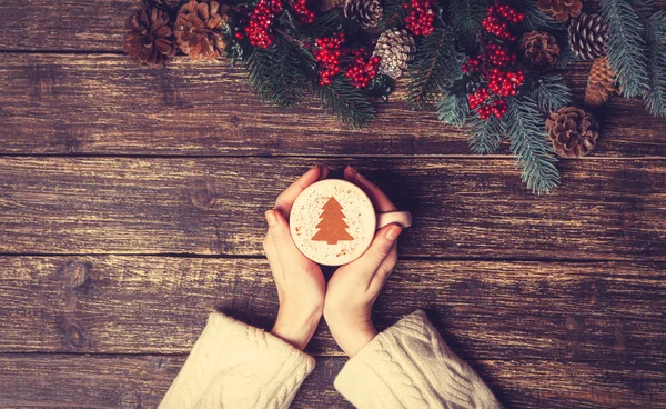 Female holding cup of coffee with cream christmas tree on a tabl — Stock Photo, Image