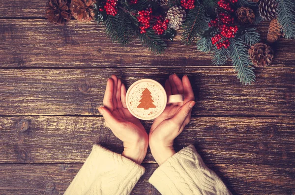 Femme tenant tasse de café avec arbre de Noël crème sur une table — Photo