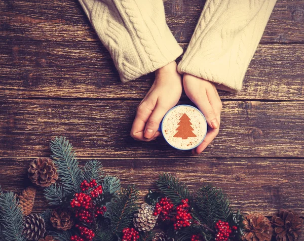 Female holding cup of coffee with cream christmas tree on a tabl — Stock Photo, Image