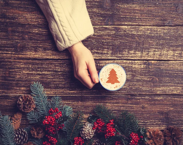 Female holding cup of coffee with cream christmas tree on a tabl — Stock Photo, Image