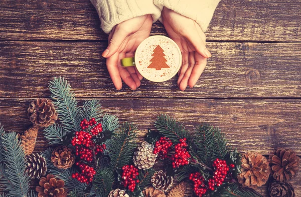 Female holding cup of coffee with cream christmas tree on a tabl — Stock Photo, Image