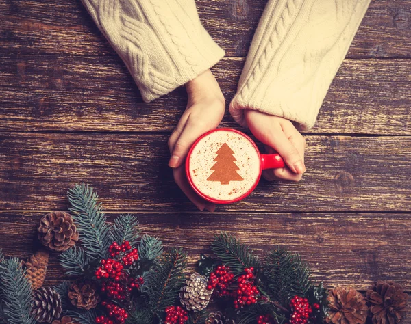 Femme tenant tasse de café avec arbre de Noël crème sur une table — Photo