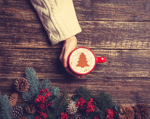 Feminino segurando xícara de café com árvore de Natal creme em uma mesa — Fotografia de Stock