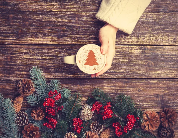 Female holding cup of coffee with cream christmas tree on a tabl — Stock Photo, Image