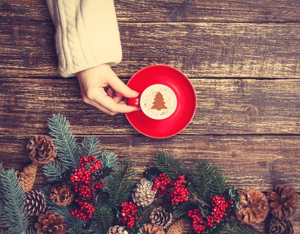 Femme tenant tasse de café avec arbre de Noël crème sur une table — Photo