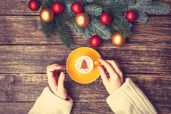 Female holding cup of coffee with cream christmas tree on a tabl — Stock Photo, Image