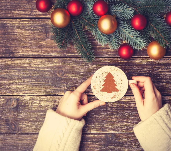 Female holding cup of coffee with cream christmas tree on a tabl — Stock Photo, Image