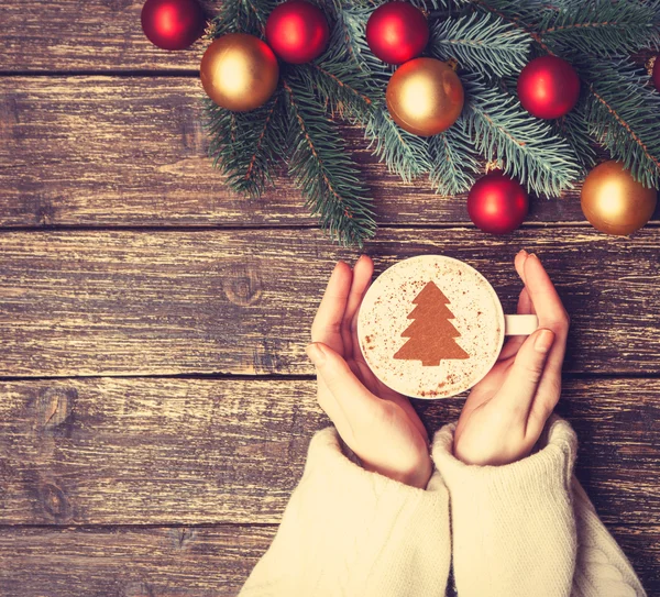 Female holding cup of coffee with cream christmas tree on a tabl — Stock Photo, Image