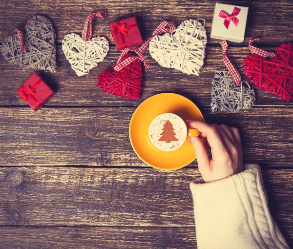 Frau hält Tasse Kaffee mit cremefarbenem Weihnachtsbaum auf einem Tisch — Stockfoto