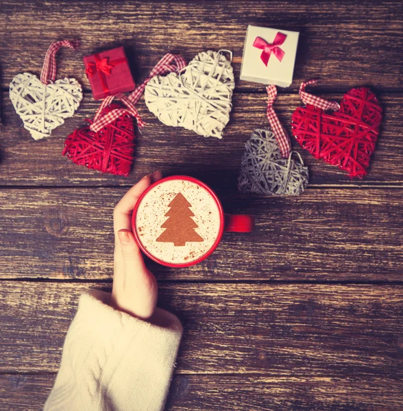 Femme tenant tasse de café avec arbre de Noël crème sur une table — Photo