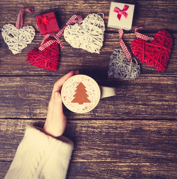 Frau hält Tasse Kaffee mit cremefarbenem Weihnachtsbaum auf einem Tisch — Stockfoto