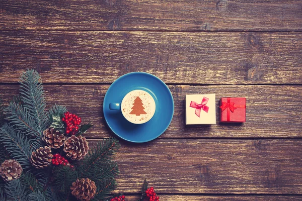 Kopje koffie met crème kerstboom en gift op een tabel. — Stockfoto