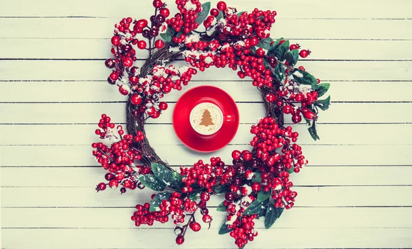 Stechpalme-Weihnachtskranz mit Cappuccino auf Holztisch. — Stockfoto