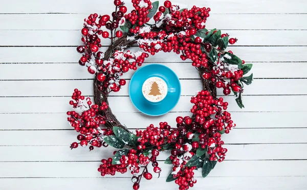 Holly christmas wreath with cappuccino on wooden table. — Stock Photo, Image