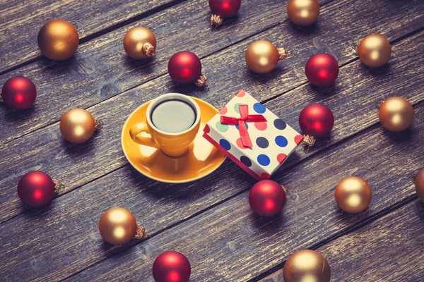 Cup of coffee and christmas balls and gift on wooden table. — Stock Photo, Image