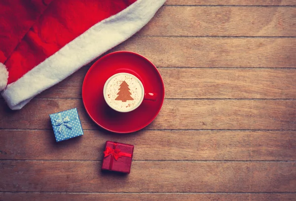 Cappuccino met kerst hoed en gift op houten tafel. — Stockfoto