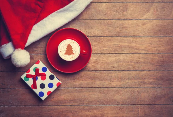 Cappuccino con cappello di Natale e regalo sulla tavola di legno . — Foto Stock