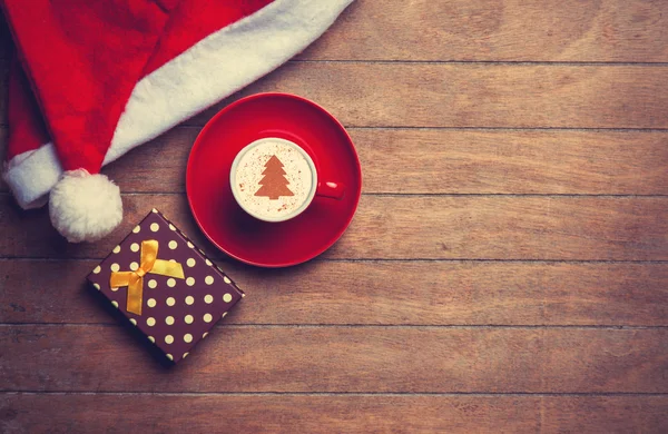 Cappuccino med jul hatt och present på träbord. — Stockfoto