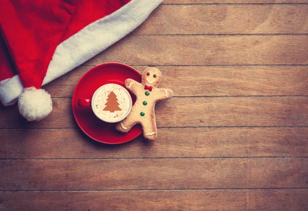 Cappuccino with christmas hat and gingerbread man on wooden tabl — Stock Photo, Image