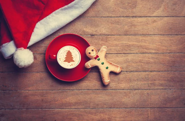 Cappuccino com chapéu de Natal e homem de gengibre na mesa de madeira — Fotografia de Stock