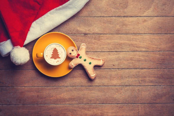 Cappuccino com chapéu de Natal e homem de gengibre na mesa de madeira — Fotografia de Stock