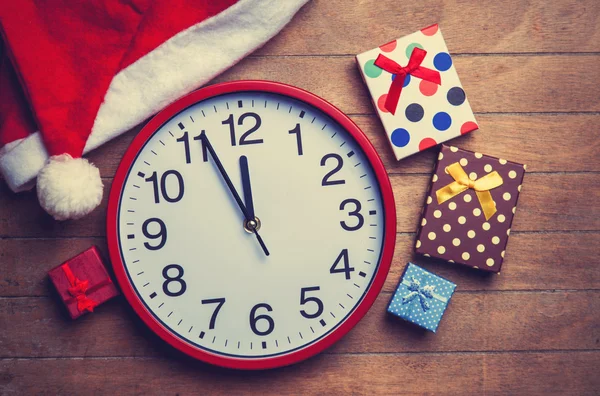 Relógio e chapéu de Natal com presentes na mesa de madeira . — Fotografia de Stock