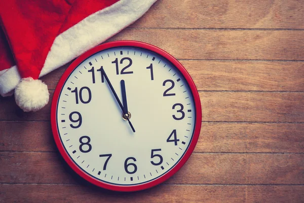 Clock and christmas hat on wooden table. — Stock Photo, Image