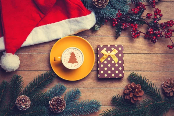 Cup of coffee and gift box with pine and hat on wooden table. — Stock Photo, Image