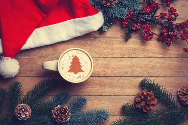 Cappuccino, karácsonyi kalap és a fából készült asztal fenyő. — Stock Fotó