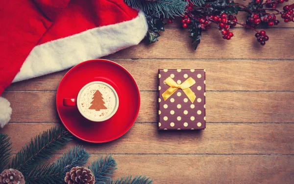 Cappuccino met kerst hoed en pijnbomen op houten tafel. — Stockfoto