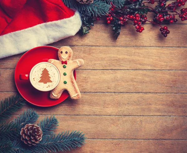 Cappuccino with gingerbread man and pine branch on wooden table. — Stock Photo, Image