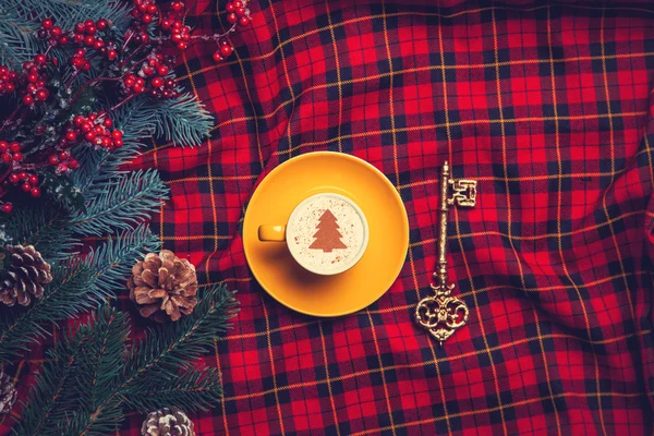 Tartan zemin üzerine anahtarıyla cappuccino ve çam dalı