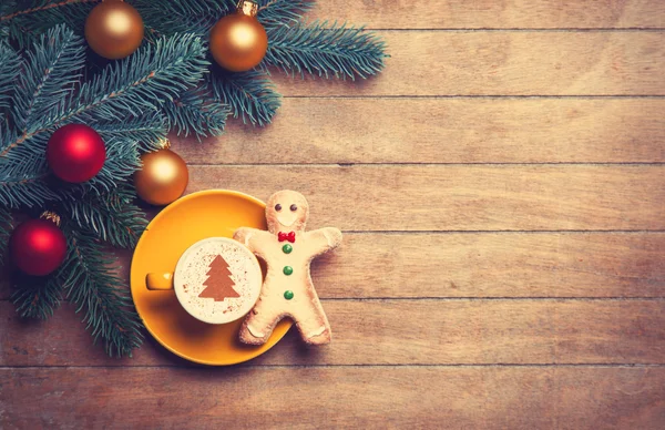 Cappuccino with gingerbread man and pine branch on wooden table. — Stock Photo, Image