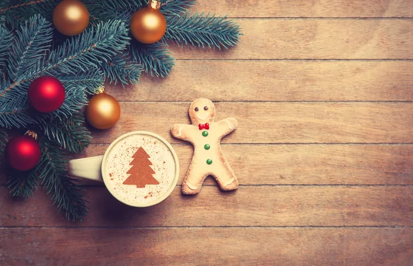 Cappuccino with gingerbread man and pine branch on wooden table. — Stock Photo, Image