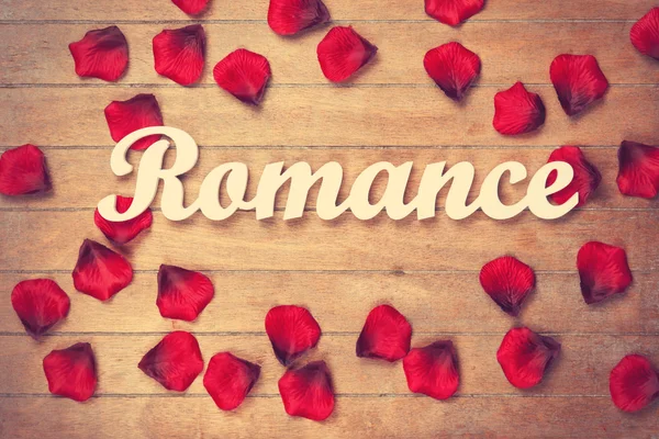 Word Romance and petals on wooden table. — Stock Photo, Image