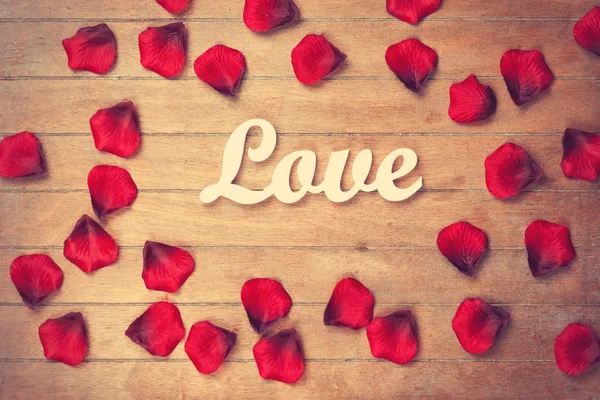 Wort Liebe und Blütenblätter auf Holztisch — Stockfoto