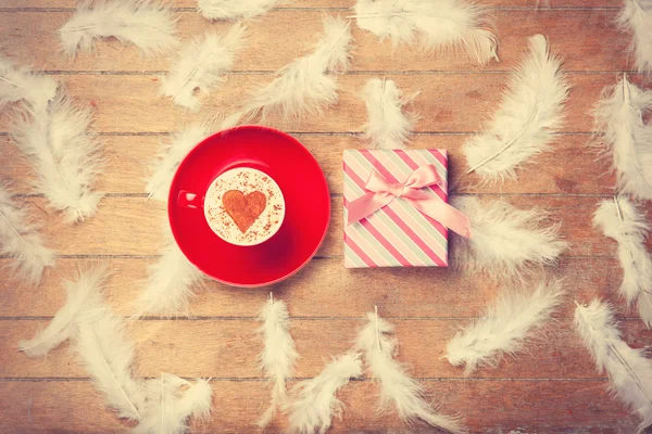 Coffee and feathers with gift on wooden background. — Stock Photo, Image