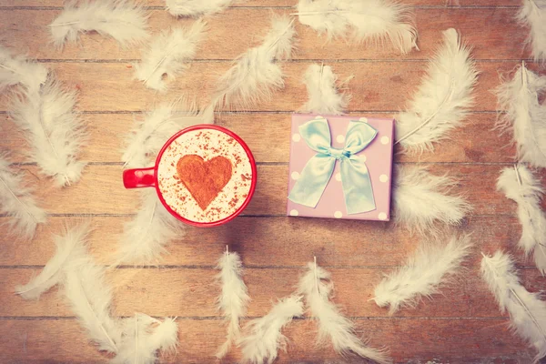 Coffee and feathers with gift on wooden background. — Stock Photo, Image