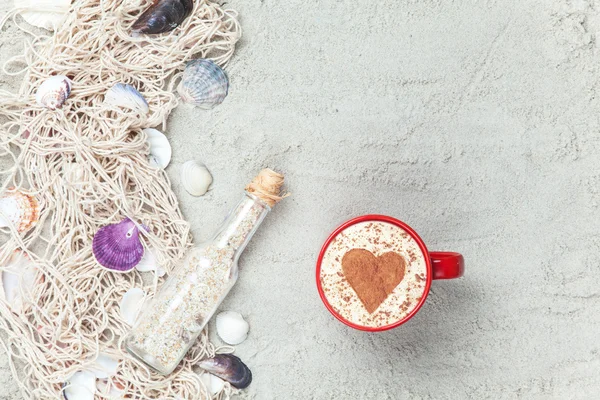 Cup, flaska och nätet med skal på sand — Stockfoto