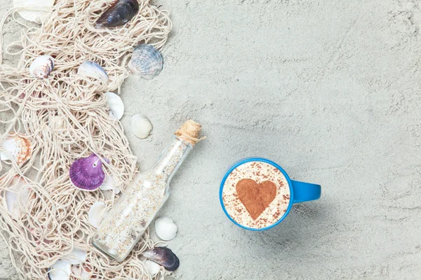 Cup, flaska och nätet med skal på sand — Stockfoto