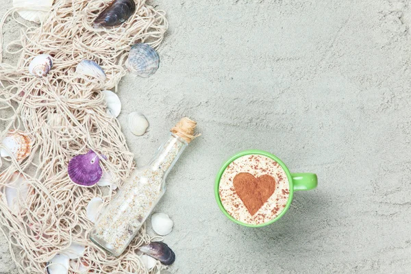 Cup, fles en net met schelpen op zand — Stockfoto
