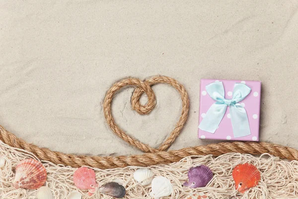 Caja de regalo y cuerda en forma de corazón cerca de la red y conchas — Foto de Stock