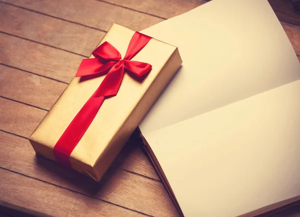 Opened book and gift box on a wooden table. — Stock Photo, Image