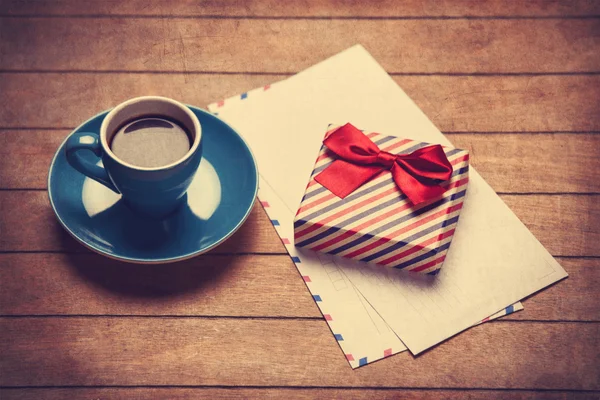 Šálek kávy a dárkové krabice s obálky na dřevěný stůl. — Stock fotografie
