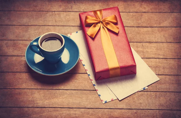 Kopje koffie en geschenk doos met enveloppen op een houten tafel. — Stockfoto